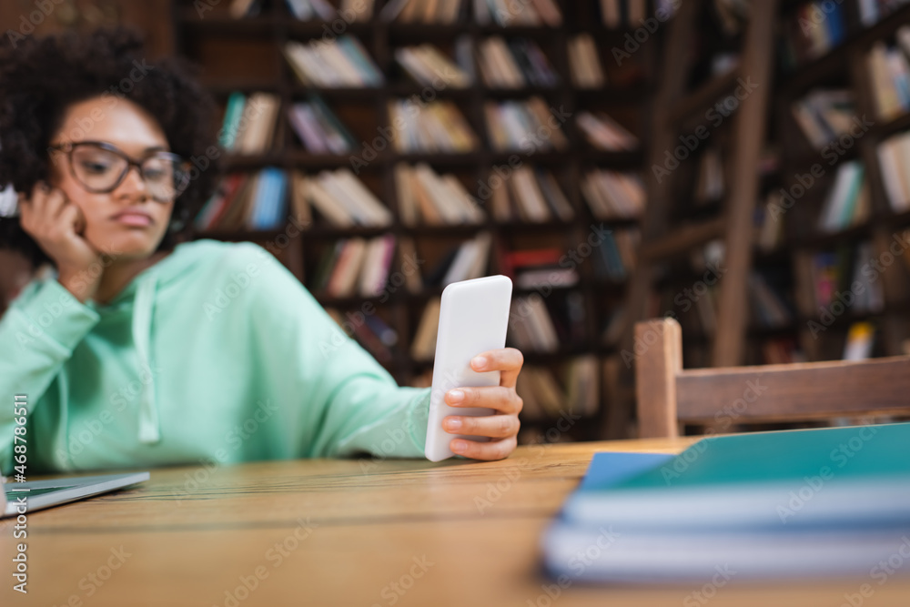 blurred african american student in eyeglasses using smartphone blurred african american student in eyeglasses using smartphone