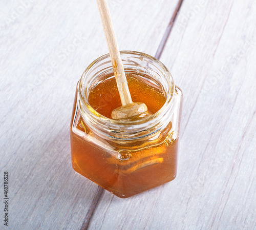 Fresh delicious transparent honey in a glass jar with a spoon for honey. Honey drips from the spoon. A jar of honey on a light wooden background.
