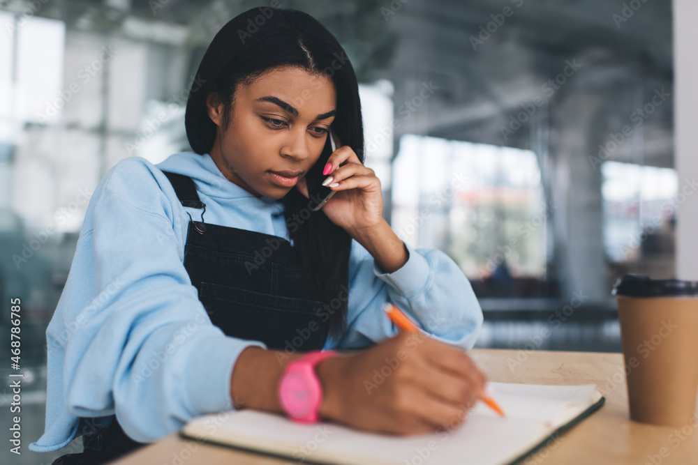 Obraz premium Black girl writing and talking on smartphone
