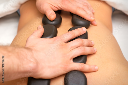 Young caucasian woman receiving back massage with black stones by masseur in spa salon. A woman getting a spa treatment