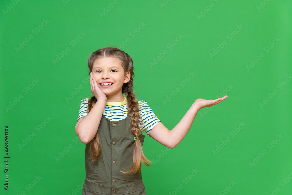 A little girl points to an advertisement. Copy space. Green isolated background. A little girl points to an advertisement. Copy space. Green isolated background.