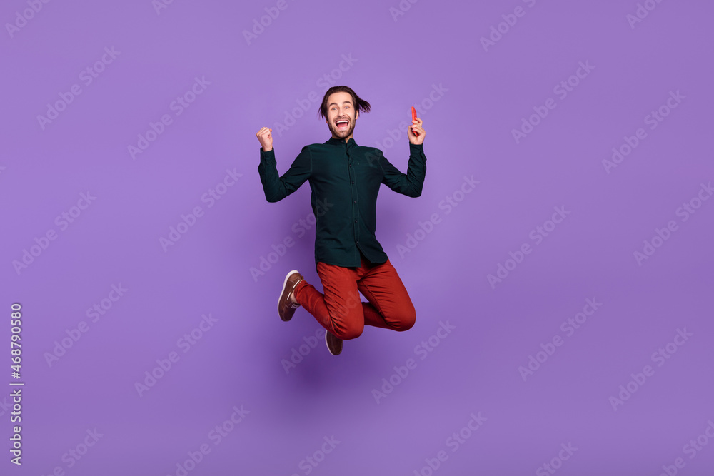 Photo of funky lucky young guy dressed smart casual clothes writing modern gadget jumping high smiling isolated violet color background