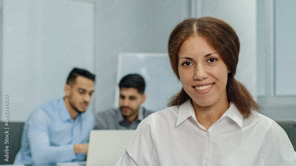 Smiling female leader manager coach speaker looking at camera. Friendly businesswoman greeting or welcoming new worker in modern business office with multicultural multiethnic professionals team