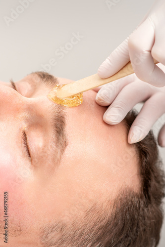 Fototapeta Naklejka Na Ścianę i Meble -  Beautician applying wax paste between eyebrows during the procedure of waxing in the beauty salon