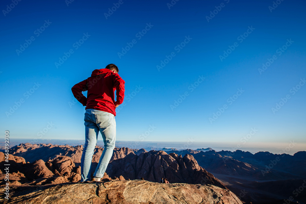 A man in a red jacket stands facing the rising sun on Mount Sinai in Egypt.