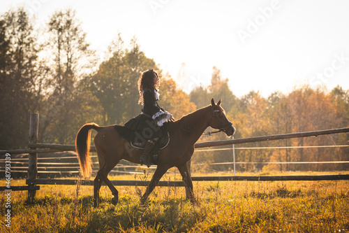 Portrait of a mature woman in a steampunk costume on a horse against the backdrop of an autumn landscape. Lady rides a horse through a fenced pasture