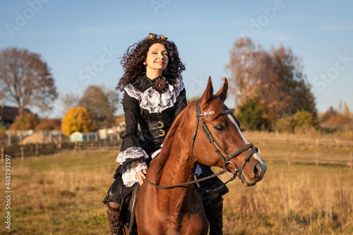 Portrait of a mature woman in a steampunk costume on a horse against the backdrop of an autumn landscape.