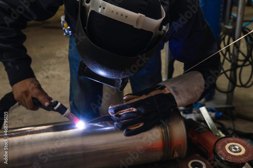 Welder is welding the steel in the factory. Weld the steel in dark. Workers wearing industrial uniforms and welding masks at a welding factory protect from welding sparks. Occupational safety concept