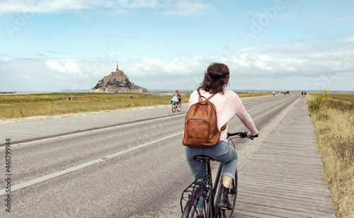 Young woman on bicycle wearing backpack with mont saint michel in background © artshake