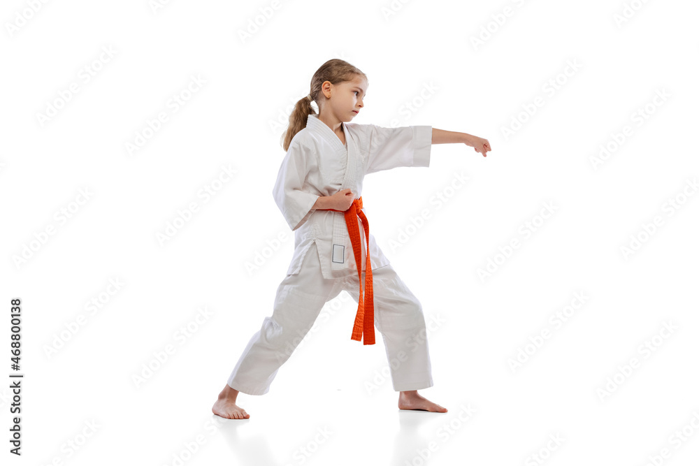 Studio shot of little girl, young karate training alone isolated over white background. Concept of sport, education, skills Studio shot of little girl, young karate training alone isolated over white background. Concept of sport, education, skills