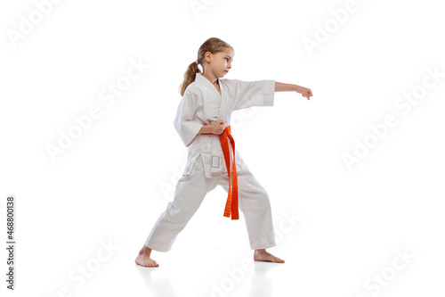 Studio shot of little girl, young karate training alone isolated over white background. Concept of sport, education, skills