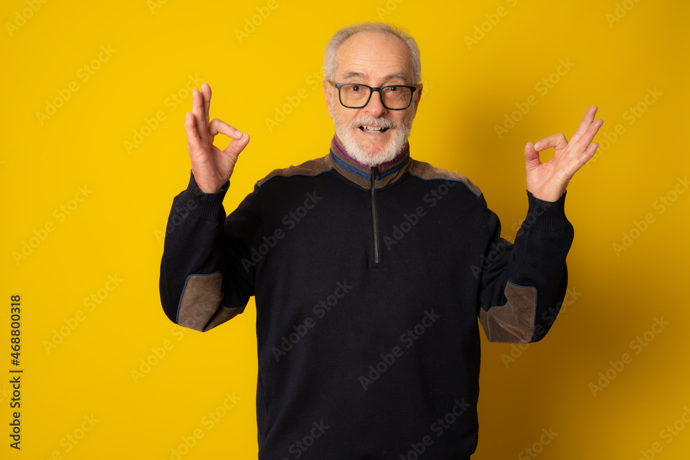 Amazed mature man wearing winter clothing with okay sign isolated over yellow background. Amazed mature man wearing winter clothing with okay sign isolated over yellow background.