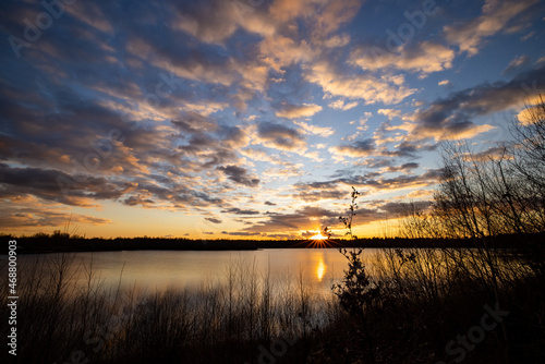 a beautiful blue lake with some tree silhouettes in the foreground under a dramatic sunset sky. High quality photo