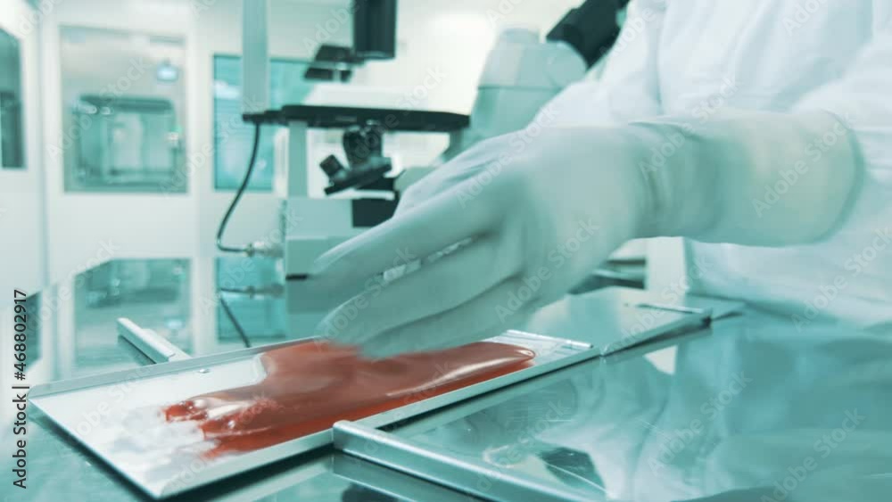 Close-up shot of hands, in protective gloves, putting a blood bag in blood bag cassette, to store and protect. In the background visible a microscope. Close-up shot of hands, in protective gloves, putting a blood bag in blood bag cassette, to store and protect. In the background visible a microscope.