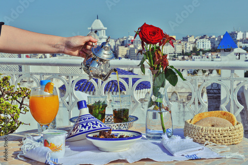   a woman holding in hand silver vintage teapot and pouring traditional mint sweet moroccan tea. Arabian hospitality and service.