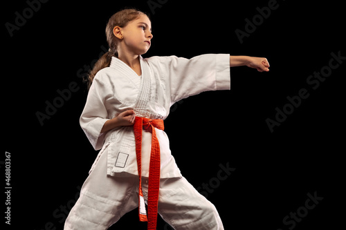 One little girl, young karate in kimono practicing isolated over dark background. Concept of sport, education, skills
