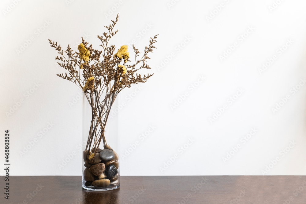 Stylish modern dried flower arrangement in a glass vase with pebbles in it on a brown wooden table. Boho style, morning sunlight in minimal home Stylish modern dried flower arrangement in a glass vase with pebbles in it on a brown wooden table. Boho style, morning sunlight in minimal home