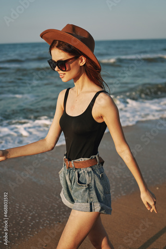 cheerful woman in sunglasses and a hat walks along the ocean