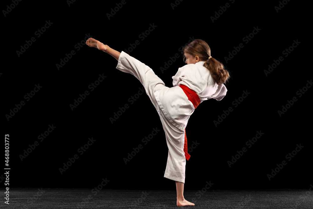 Portrait of little girl, young karate practicing alone isolated over dark background. Concept of sport, education, skills