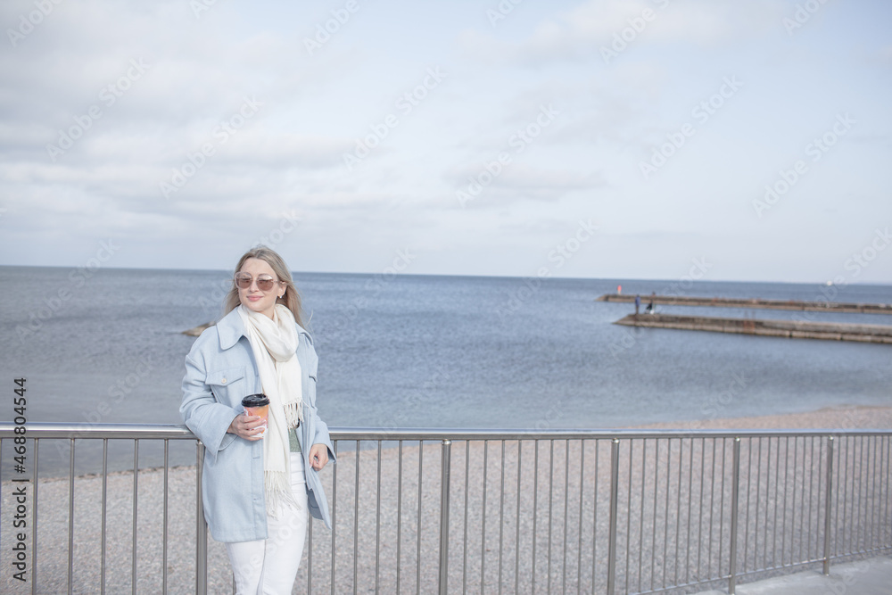 Beautiful woman dressed woolen blue jacket, white scarf and trousers walking in the beach, reston and enjoy the time is in with you, against the shore of the beach at background sea and sky