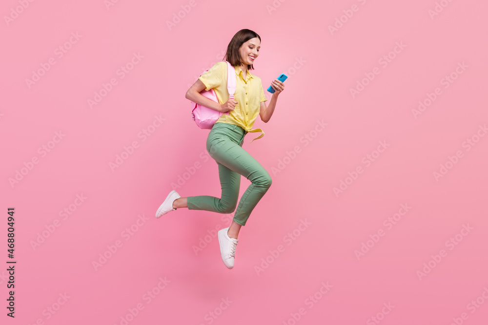 Full size profile side photo of young girl happy smile use cellphone jump up isolated over pink color background
