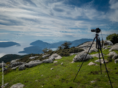 A photographer's camera and tripod on top of a mountain with a panoramic view of the sea and islands.
