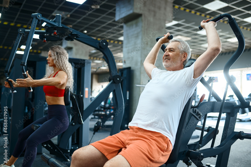 Old man on exercise machine, female trainer, gym