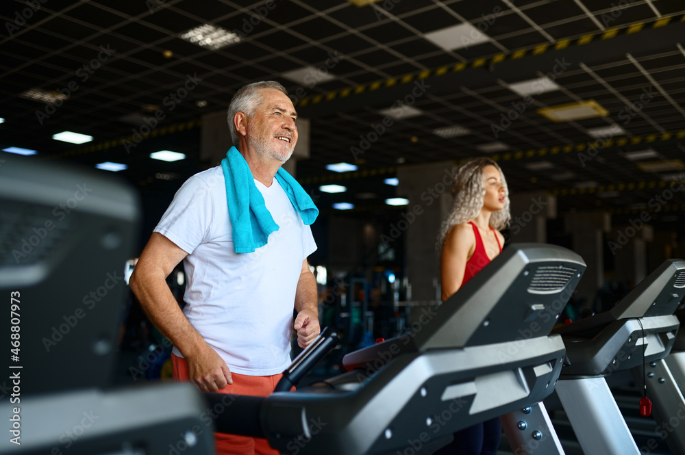 Elderly man and female trainer on treadmill in gym Elderly man and female trainer on treadmill in gym