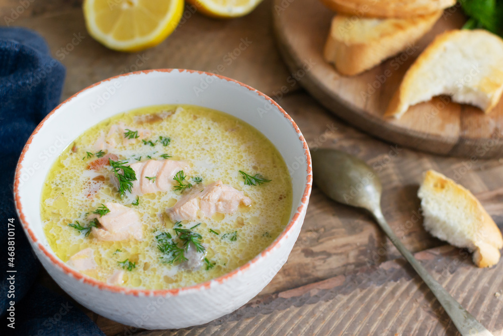 Salmon and cream fish soup in a white bowl with a spoon and a few slices of bread. Lohikeitto is a traditional Finnish and Karelian soup. Rustic style.