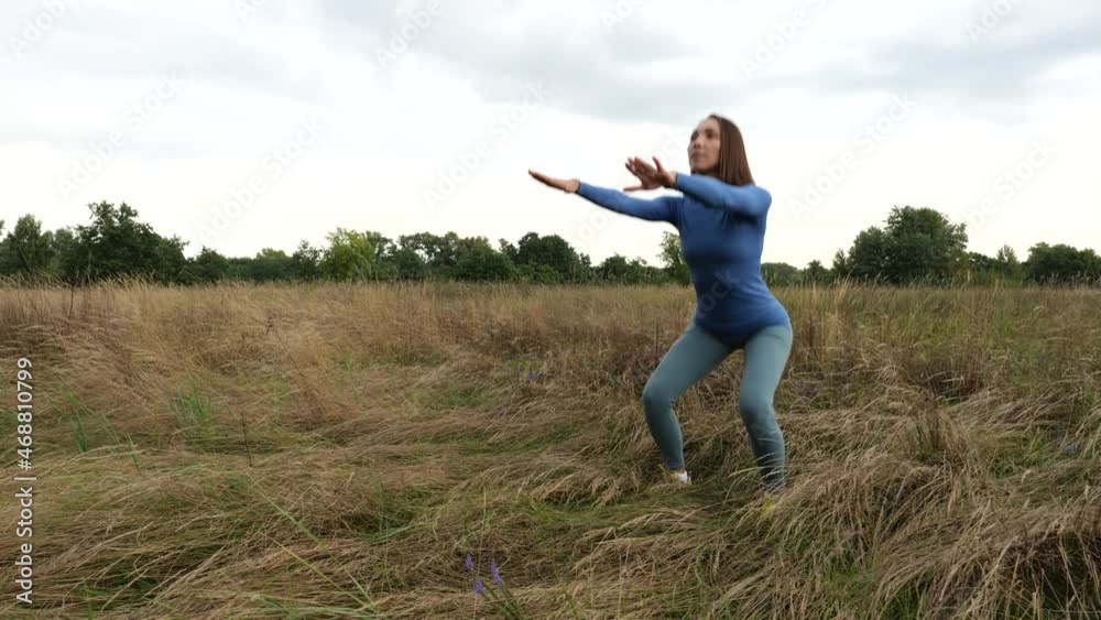 Young athletic woman squats in a dry field in nature. Activity, healthy lifestyle Young athletic woman squats in a dry field in nature. Activity, healthy lifestyle