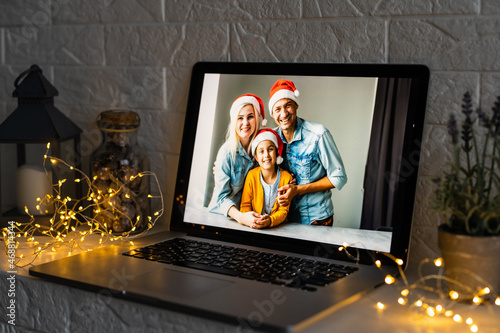Happy parents hugging cute small kid daughter holding present giving Christmas gift to web camera during virtual family social meeting on video conference call party at home, laptop webcam view.