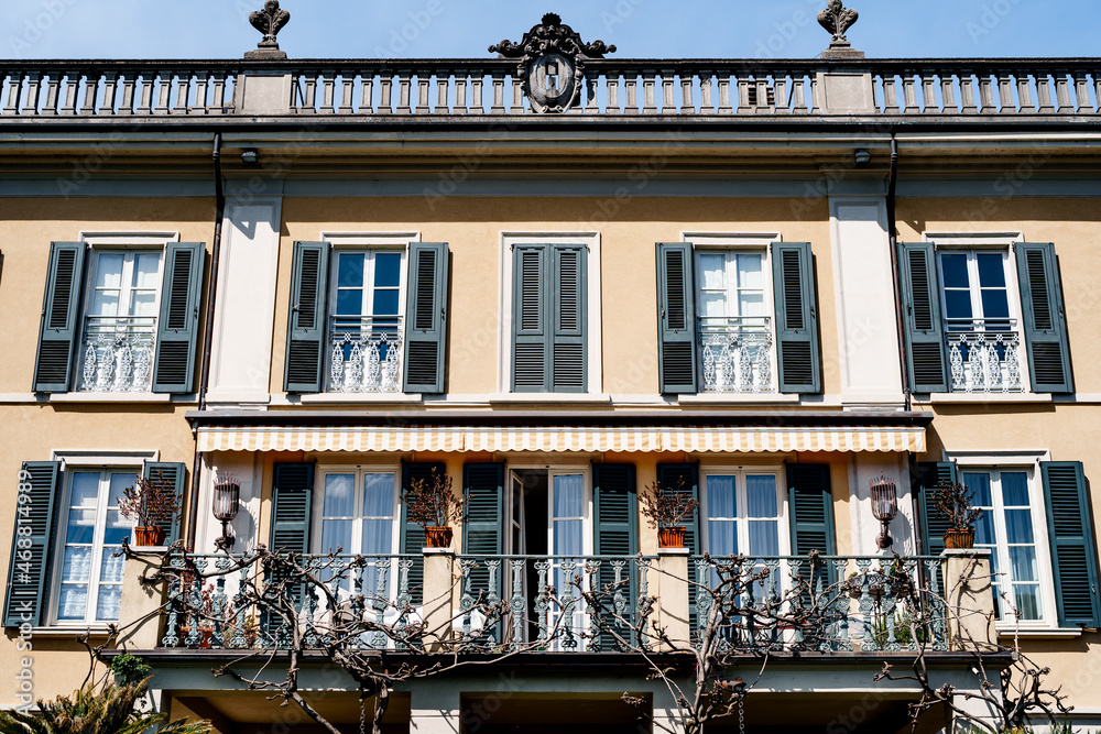 Metal balcony on the facade of the building with shutters on the windows. Como, Italy