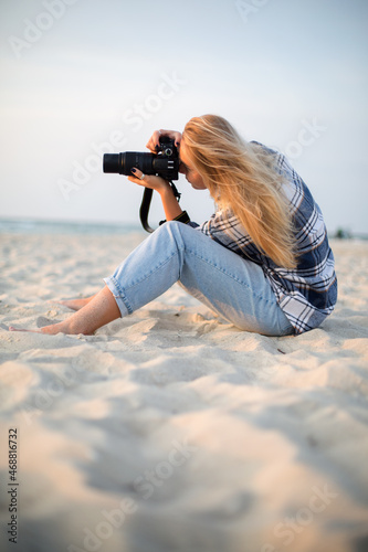 photographer girl in a sweatshirt taking a photo on a professional camera while sitting on the beach