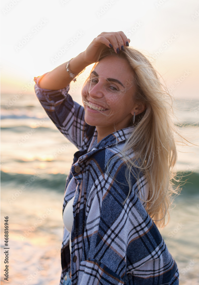 beautiful happy blonde hair girl in a sweatshirt is standing barefoot on the beach in sunrise light 