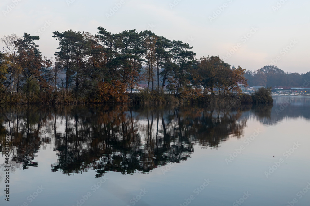 Sunrise colorful autumn hazy morning with pine trees on peninsula reflecting in the still calm IJzeren Man lake.