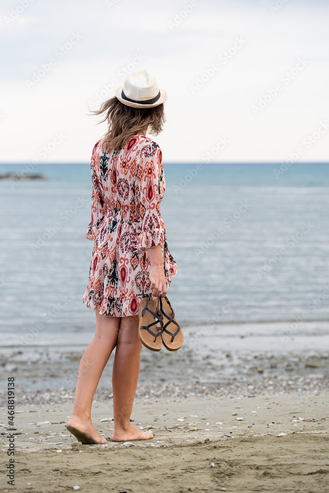 Young woman walking barefoot on a sandy beach.