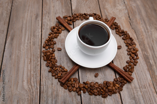 Top view of cup of coffee with cinnamon surrounded coffee beans on wooden table