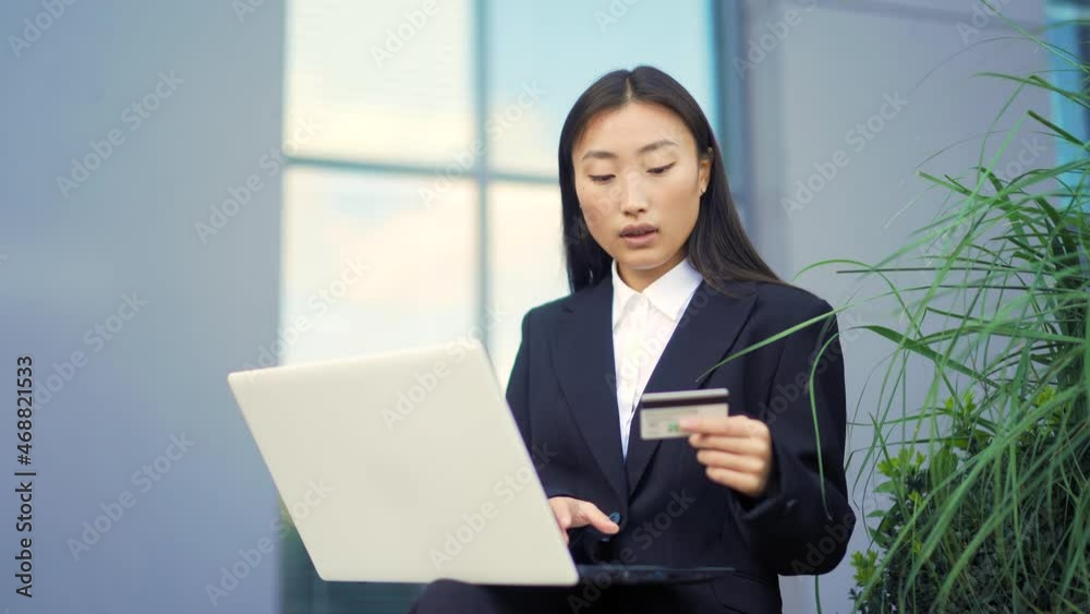 young beautiful asian business woman shopping or making payment using laptop and credit card. female office worker employee buyer on outside sits on a bench and enters data. Outdoor Center urban park young beautiful asian business woman shopping or making payment using laptop and credit card. female office worker employee buyer on outside sits on a bench and enters data. Outdoor Center urban park