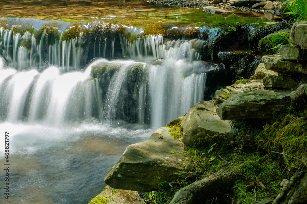 Fototapeta premium Flat rock ledge and a shallow clean clear brook with water cascading over moss covered stones