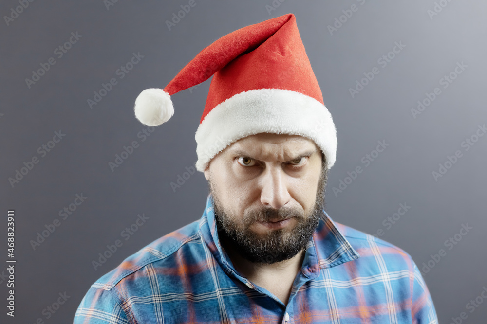 A bearded man in a Santa hat and a plaid shirt furrowed his eyebrows. Angry Santa A bearded man in a Santa hat and a plaid shirt furrowed his eyebrows. Angry Santa