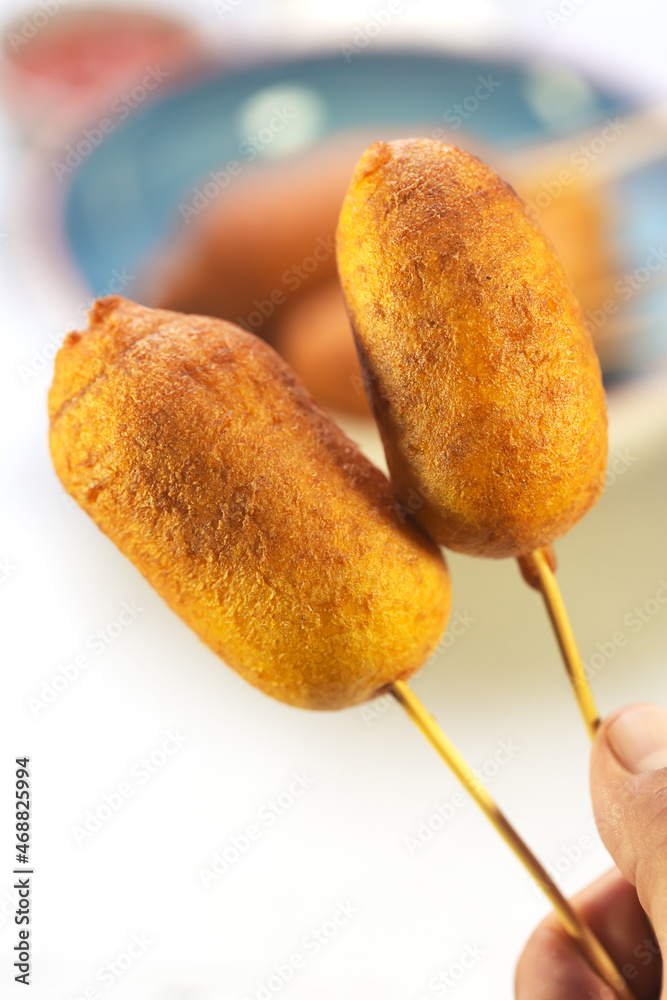 Man holds Corn two corn dogs cooked with sausage and dough - obrazy, fototapety, plakaty 