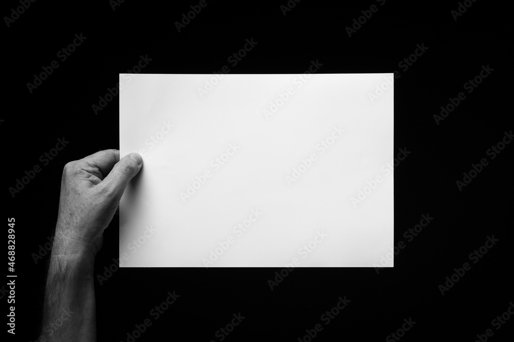 Hand holding blank sheet of paper against black background. Hand holding blank sheet of paper against black background.