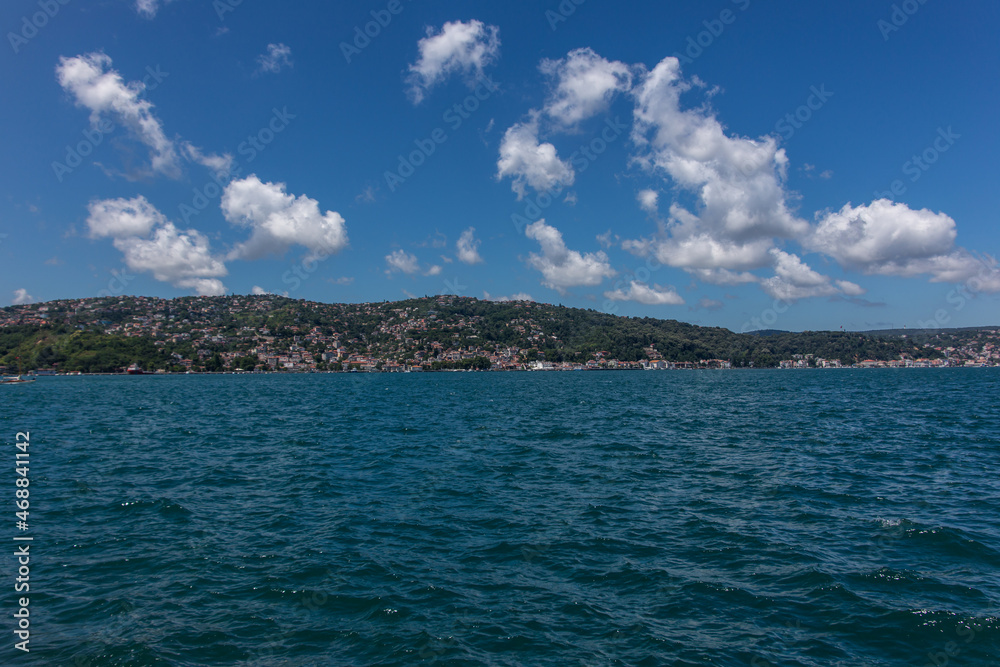 A beautiful scenic view to the green hills and houses over the blue Bosphorus under the beautiful blue sky with white cotton clouds on a sunny day.