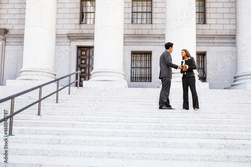 A man and woman in discussion on the exterior steps of a courthouse. Could be lawyers, business people etc.