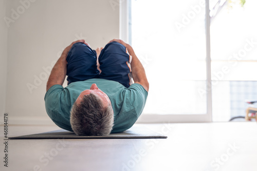 Older adult male doing stretches in a yoga studio. © lorenzophotoprojects