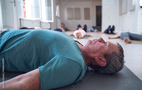 Older adult male lying on the floor during a group yoga class.