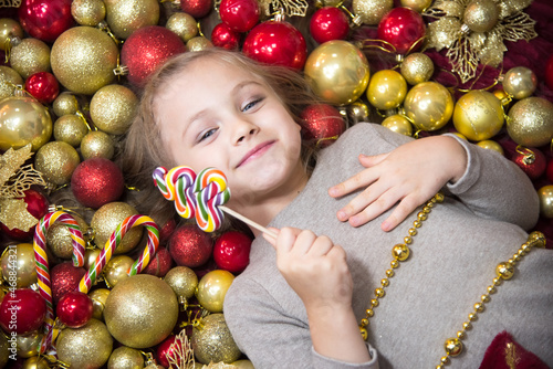 In the New Year's balls lies a blonde girl with a lollipop. Nearby are New Year's candies and balls of red and gold. Place to insert.