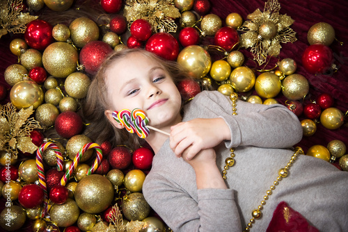 In the New Year's balls lies a blonde girl with a lollipop. Nearby are New Year's candies and balls of red and gold. Place to insert.