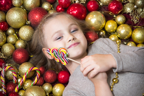 In the New Year's balls lies a blonde girl with a lollipop. Nearby are New Year's candies and balls of red and gold. Place to insert.