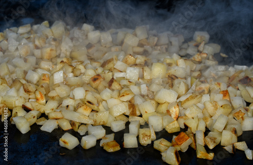 Canvas Print Hash browns being cooked on a griddle, with steam rising from the small cubed po